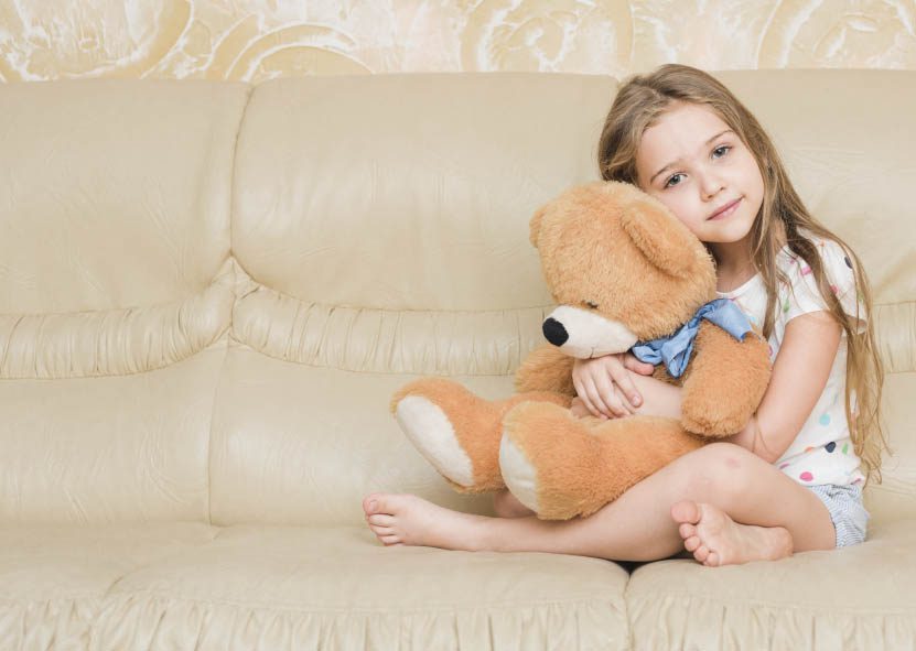 A young girl sitting on a couch hugging her teddy bear